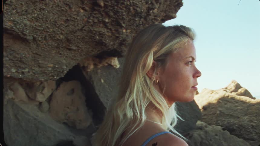 Blonde woman gazes at the sea near the rocks on the beach