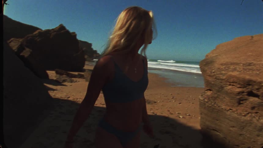 Woman walks along the beach beside a rock under the deep blue sky