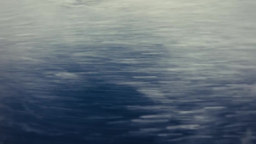 This is a fastmoving underwater or partially submerged shot that captures the turbulence and bubbles just beneath the surface of the oceanthe water transitions from dark blue deep tones to a frothy bright white near the top suggesting the motion o
