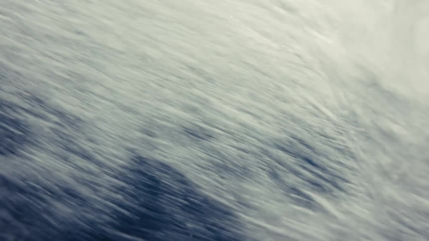 This short clip alternates between shots of the ocean surface and underwater views of a dolphinit begins with a view of a fin above the choppy whitecapped water then transitions to the dark blue depths where a dolphin is seen swimming gracefully nea