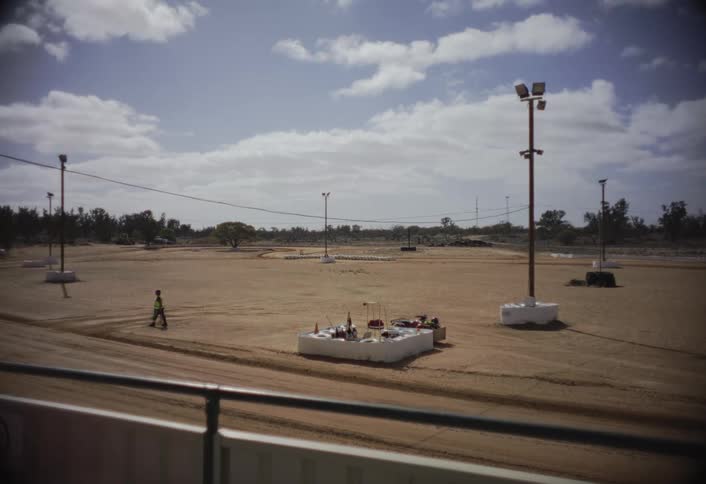 A lone flag marshal walks across a deserted dirt racetrack under a cloudy sky