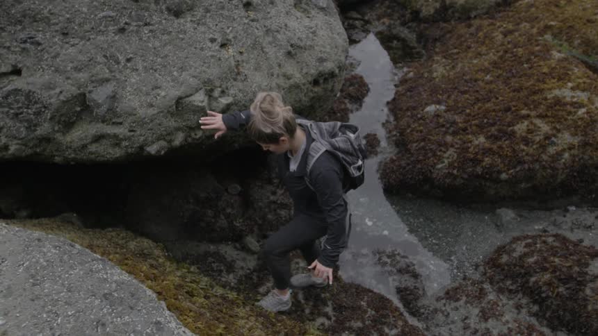 Woman hiking around large rock boulders in water