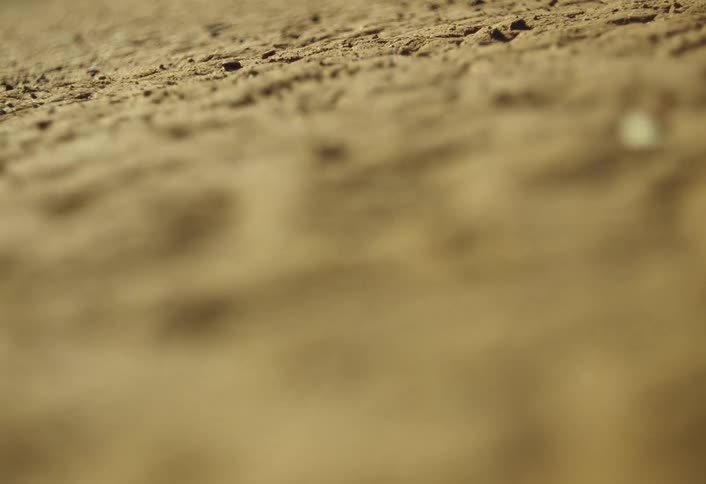 The video is a shallow depthoffield closeup shot of dry brown earth or sandthe cameras focus racks from the foreground to the midground highlighting the coarse cracked texture of the grounds surface