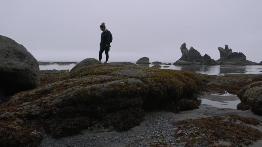 A woman is walking on the rocks by the ocean