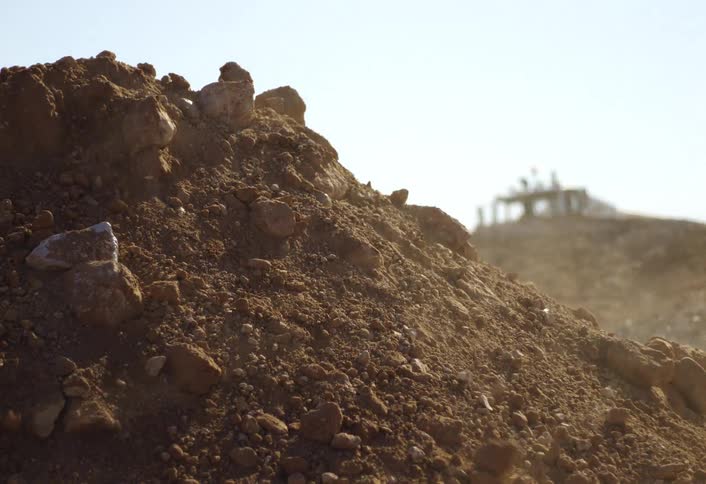 This is a closeup shot of a large pile of reddishbrown dirt and rocks likely from a construction or excavation siteinitially a cloud of dust and debris covers the lower part of the mound before clearing to reveal the texture of the soil