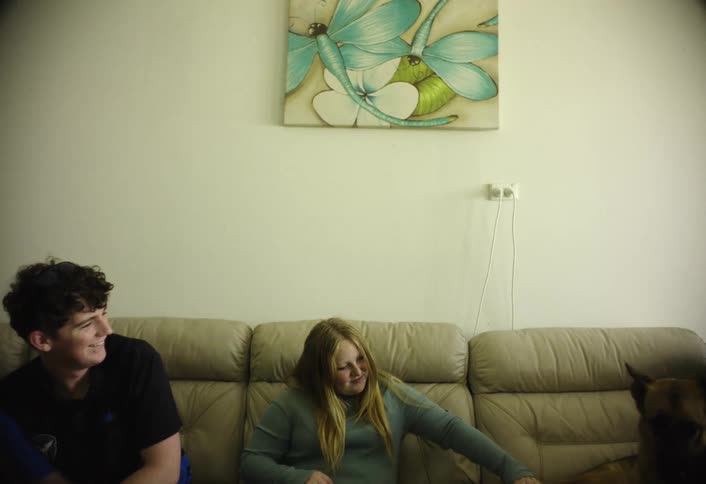 A brother and sister sit on a couch playing with their dog in a cozy living room