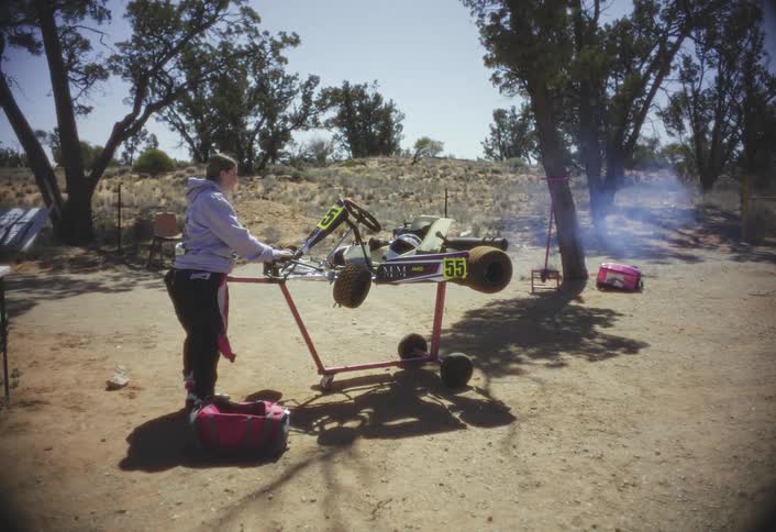 A woman repeatedly revs a go kart that is immobilized atop a rack