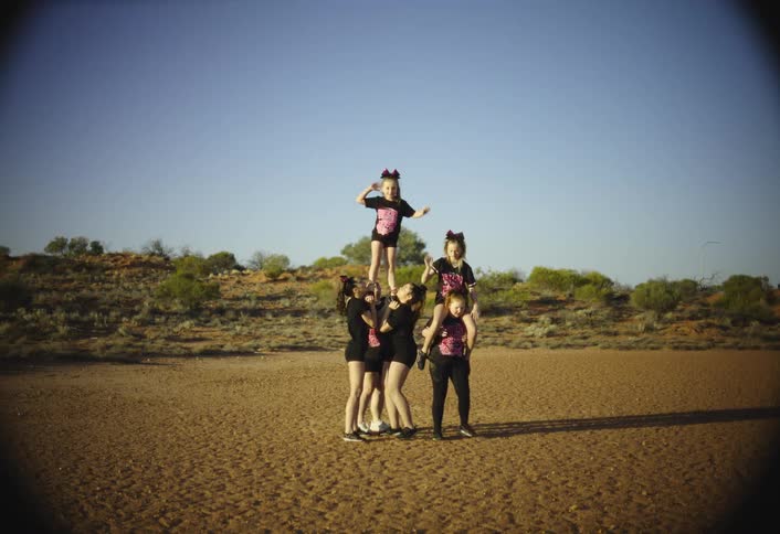 A group lifts a child high in the air for a cheer routine in a vast sunlit desert