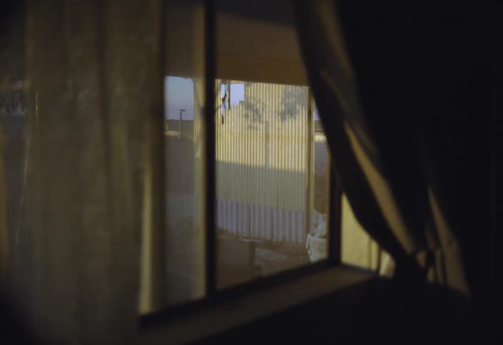 A small lot with a fence is visible from a window with the curtain drawn back