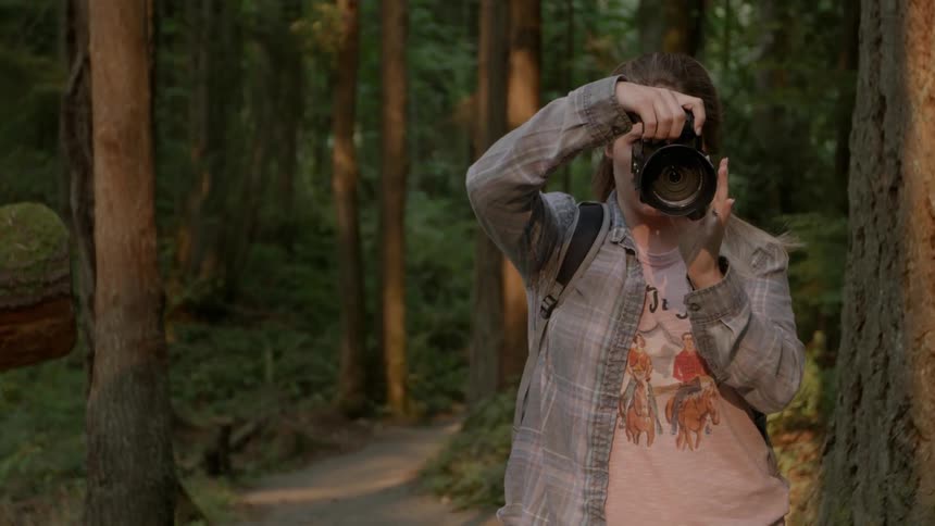 A woman standing in the forest looks through a camera lens