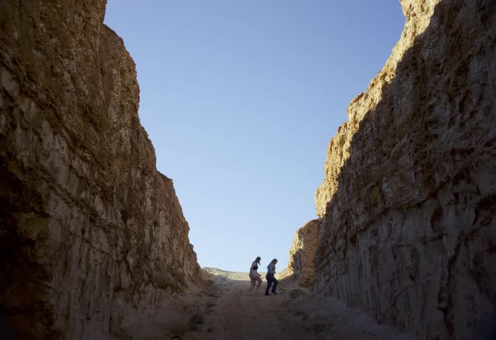 Two people dance between towering rock walls under a clear blue sky