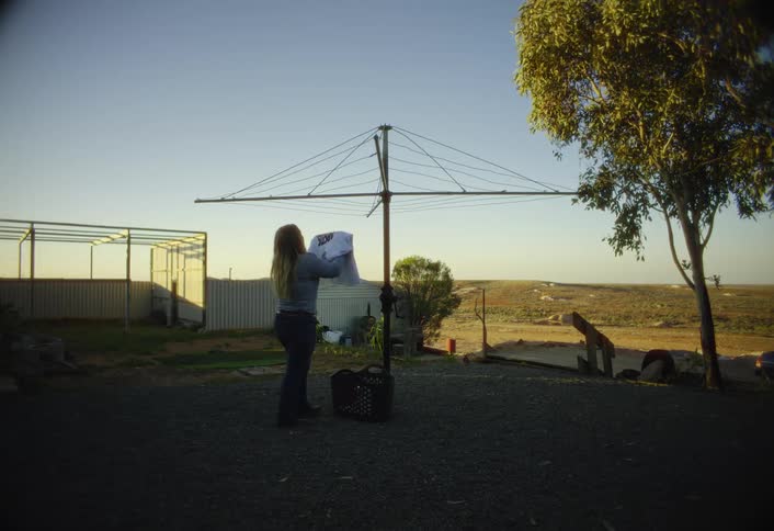 A woman hangs laundry on a clothesline in a sunny rural yard