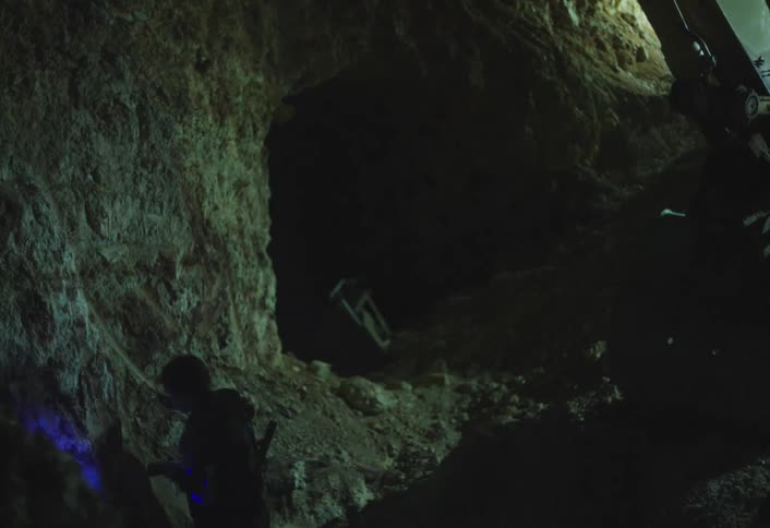 Cave explorer uses a pickaxe to make a hole inside a cave