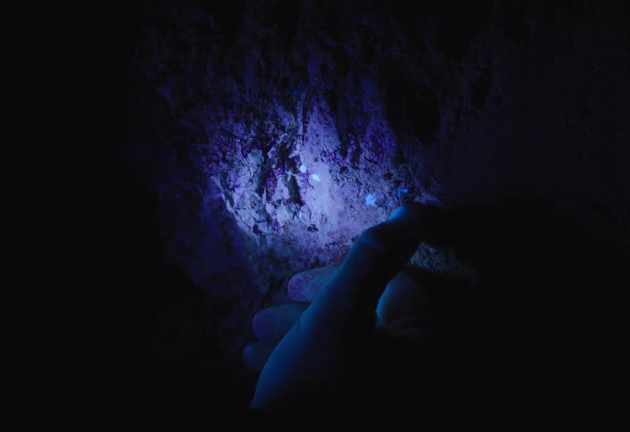 Closeup of a hand examining a rock wall under blue light in the dark
