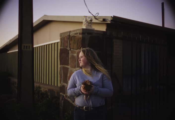 Blonde woman standing near a stone post smiles while holding a chicken