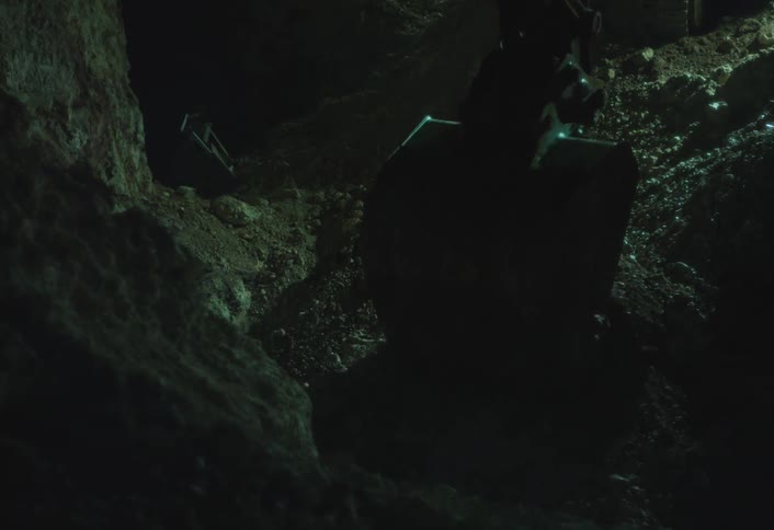 An excavator digs deep into the ground at night illuminated by its bright working lights