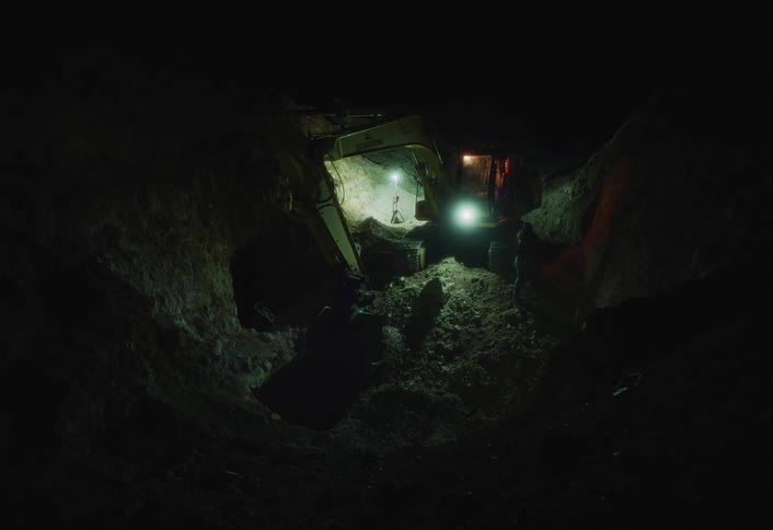 Excavator operates in a nighttime dig site illuminated by artificial lights