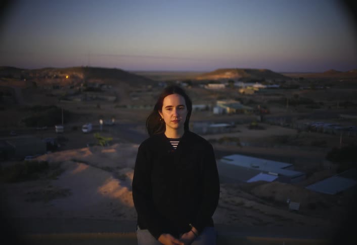 A young woman stands on a hill with the wind blowing her hair at sunset