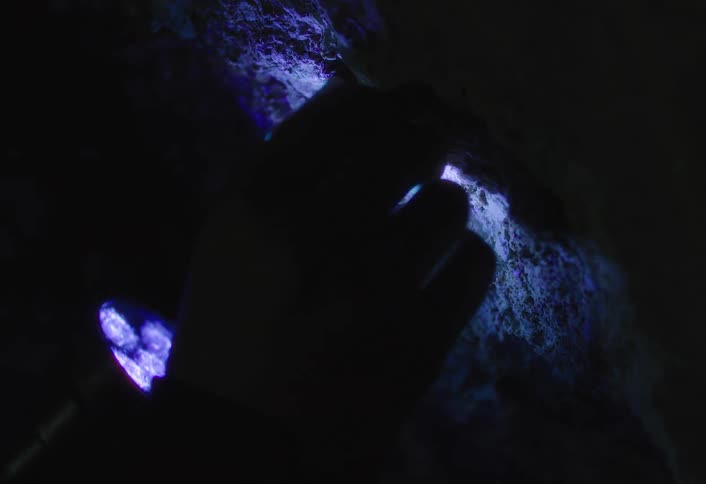 Person holding a flashlight in the dark digs at a wall with their hand