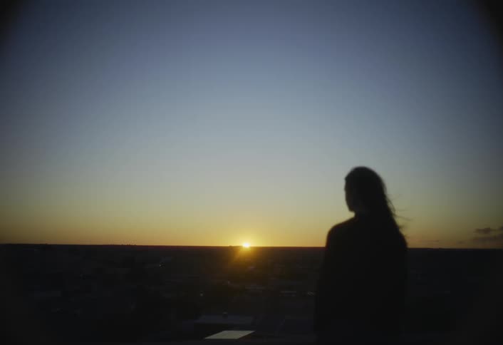 Wind blows a womans hair as she watches the sun set on the horizon