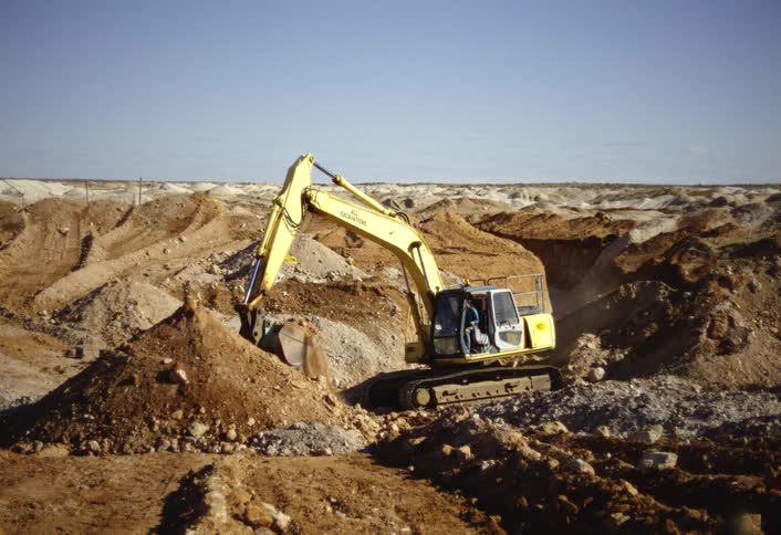 The man uses the excavator to dig up piles of dirt
