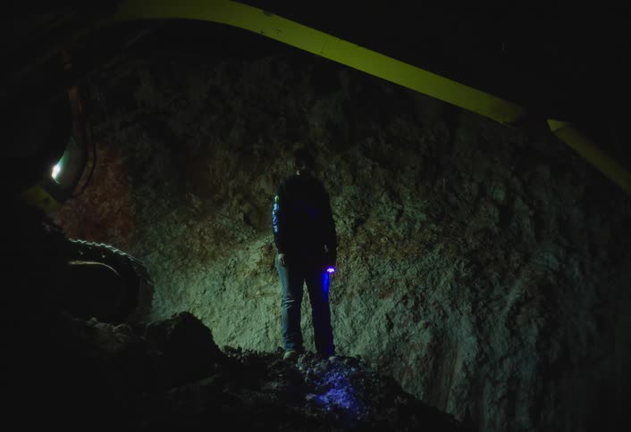 Woman holding a flashlight stands near earthmoving equipment in a tunnel and looks around