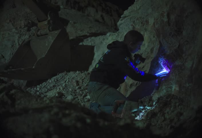 Man holds a flashlight as he drills a hole and digs inside a cave