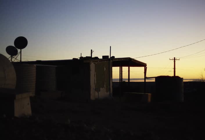 A shelter with water tanks and satellite dishes silhouettes against a colorful dawn sky
