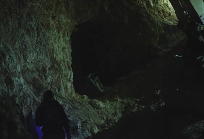 Worker mining rock illuminated by blue light in a dark tunnel