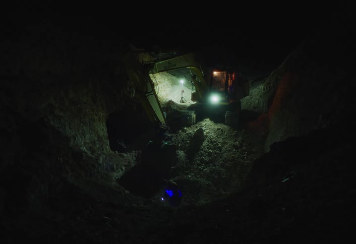 Excavator operating at a nighttime construction site lit by floodlights