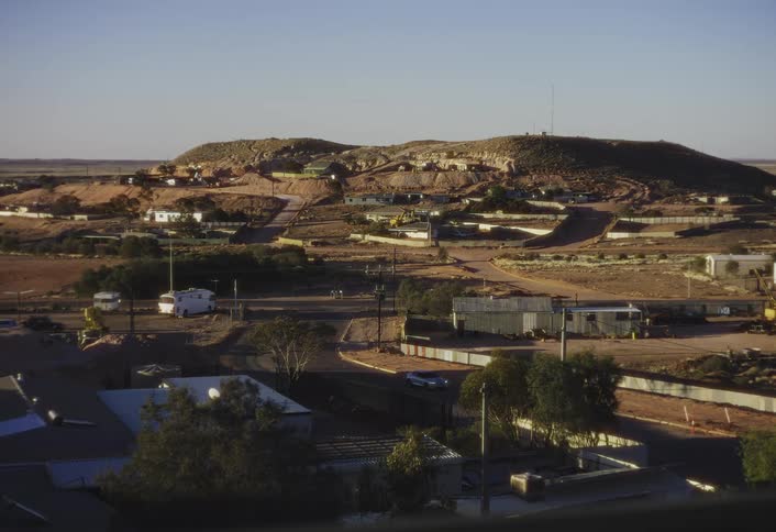 A dusty desert town of low buildings and dirt roads spreads around a sunlit hill