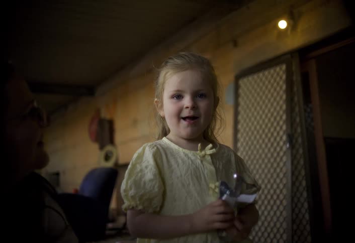 A little blonde girl in a yellow dress is looking ahead and then begins to smile