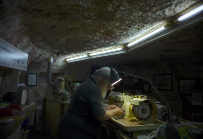 An older man operates a polishing machine in a dim underground workshop