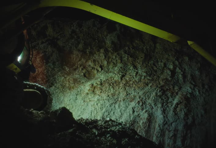 Woman walks inside a cave carrying a drill