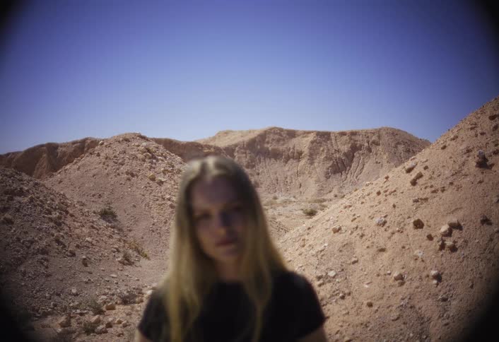 Blondehaired woman poses in an arid landscape with dirt hills under a blue sky