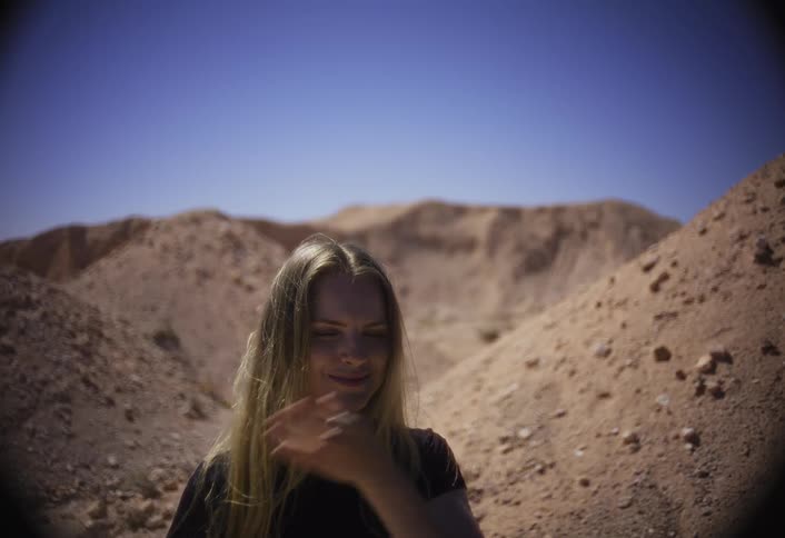 A woman standing outdoors waves her hand in front of her face