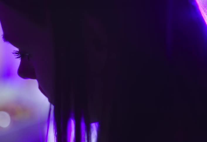 Female face in profile is softly lit by purple lights