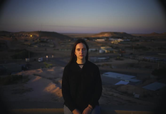 The woman sits on a hill above the small town