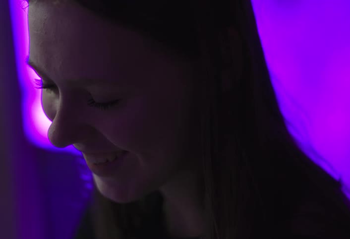 A woman smiles softly in profile against a vibrant purple lit background