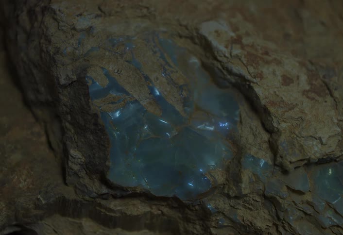 A glowing blue crystal embedded in rough brown rock
