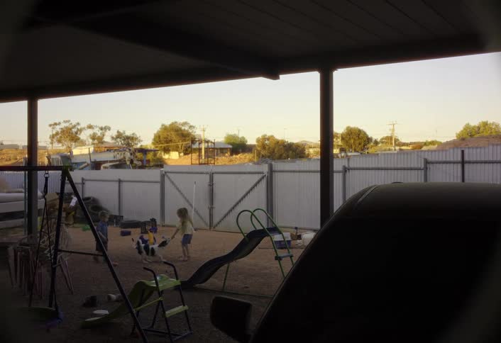 Two children play with a dog in a backyard playground at sunset
