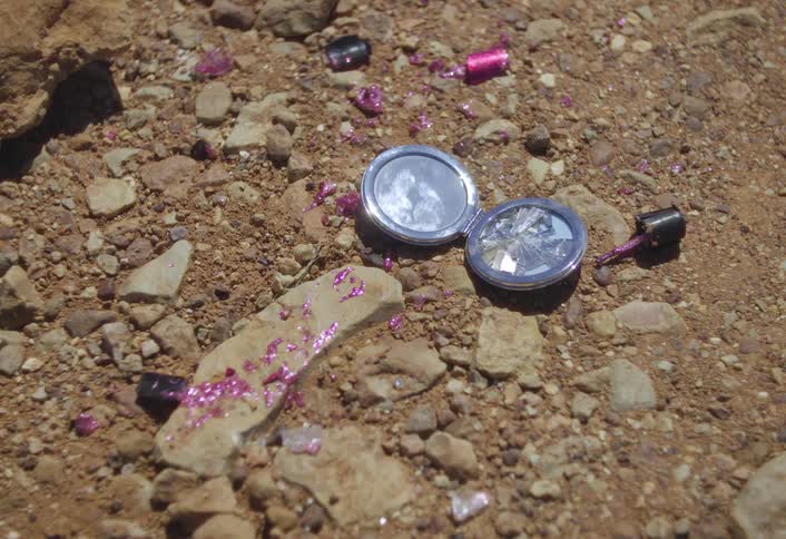 Spilled fingernail polish lies on the ground near a compact during the daytime