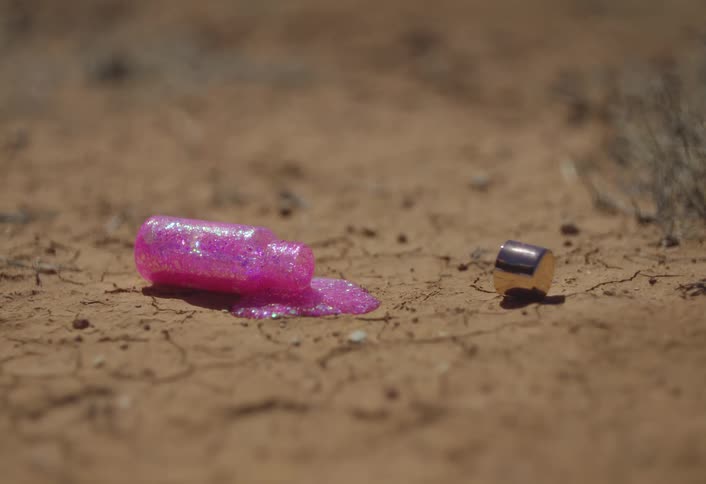 A small glass bottle of pink makeup with glitter is spill on the ground