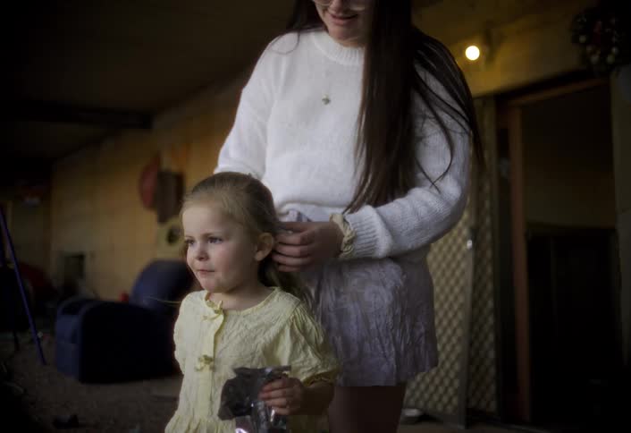 Woman fixing a girls hair on a sunlit porch