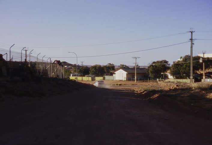The car drives on the dirt road in the rural town