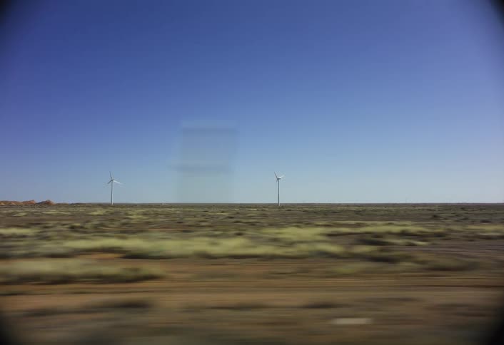 A grassy landscape containing wind turbines is passed at great speed