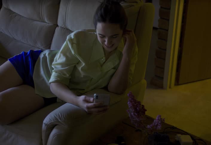 Woman relaxing on a sofa smiles while talking during a video call on her smartphone