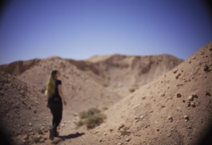 A woman hikes through a rocky desert canyon under a clear blue sky