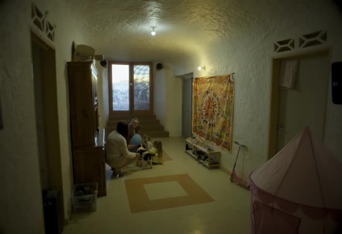 Person plays with children and dogs in a hallway lit by soft light