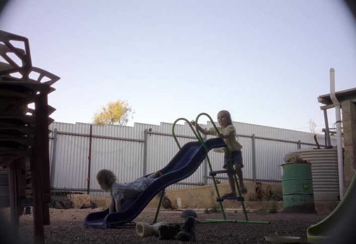 Two children playing on a slide with another child nearby walking a dog